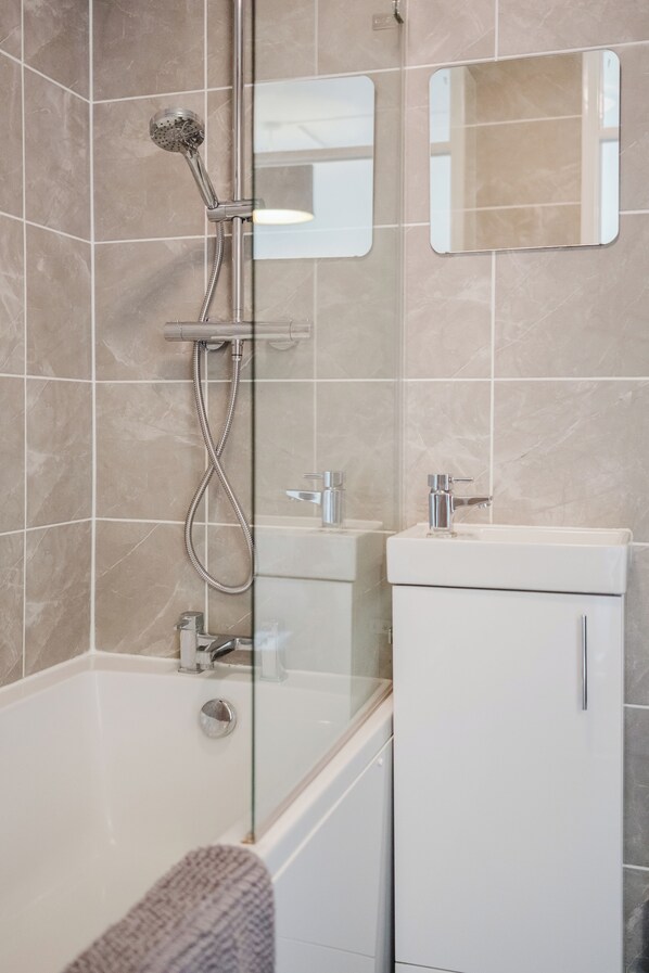 A modern bathroom with a glass-enclosed shower, a white sink, and a mirror.