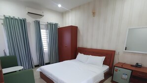 A hotel room with a bed, a desk, a chair, an air conditioning unit, and curtains.
