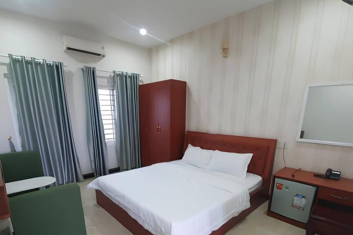Ein Hotelzimmer mit Bett, Schreibtisch, Stuhl, Klimaanlage und Vorhängen.