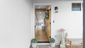 Une entrée moderne avec un escalier en bois, une pancarte de bienvenue et deux plantes en pot.
