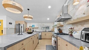 Une cuisine moderne dotée d’un grand îlot central, d’appareils électroménagers en acier inoxydable et d’un luminaire suspendu.