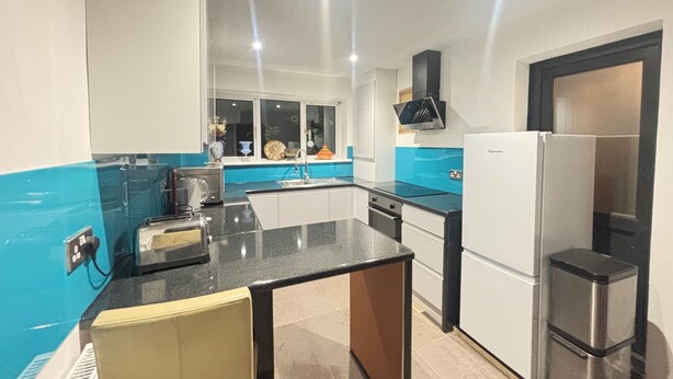 Una cocina moderna con encimera negra, armarios blancos y refrigerador de acero inoxidable.