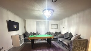 Una sala de estar con mesa de billar, sofá, televisor y candelabro.