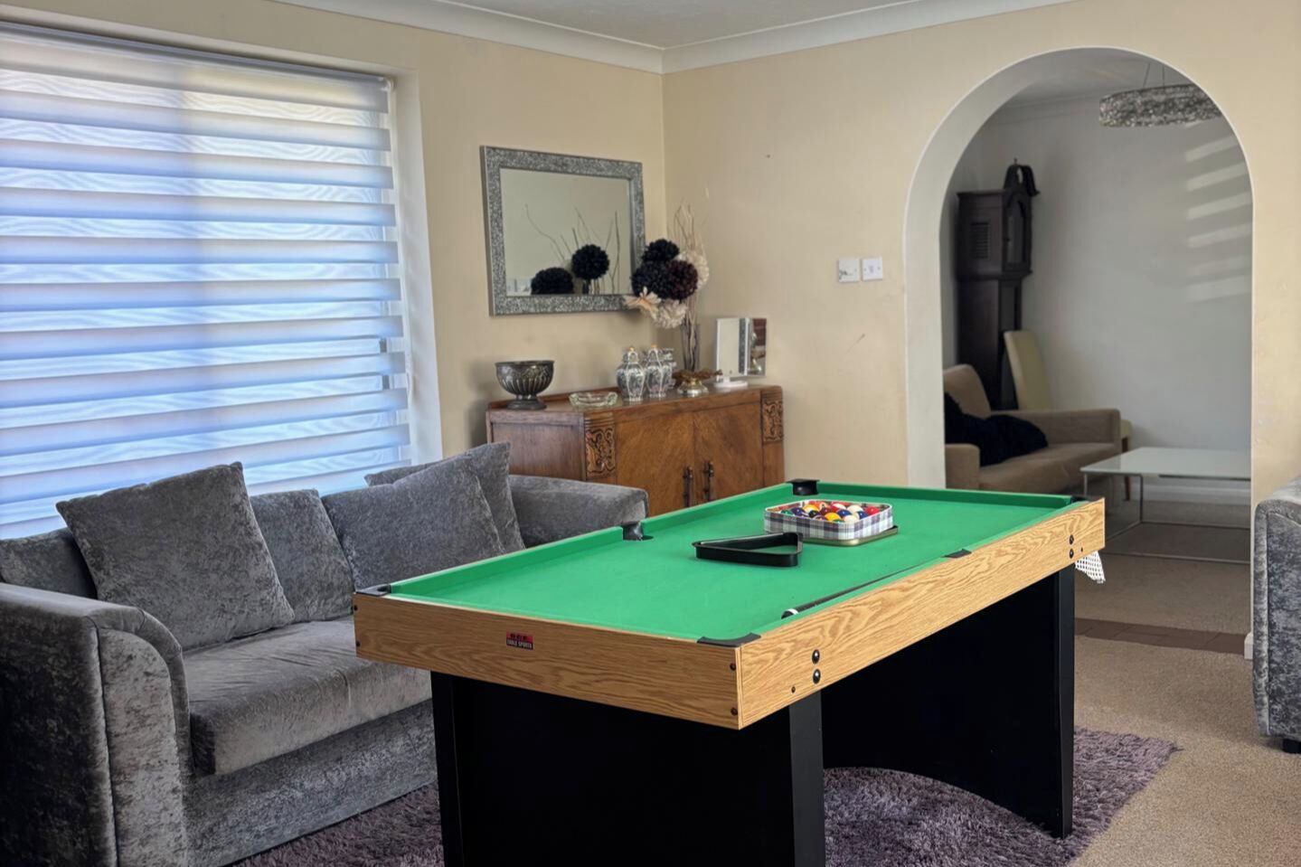 A pool table in a living room with a sofa, a cabinet, and a mirror on the wall.