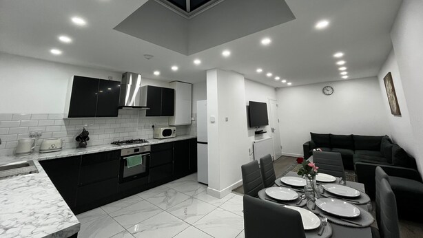 A modern kitchen with a dining area, featuring a skylight, recessed ceiling lights, and a flat-screen TV mounted on the wall.