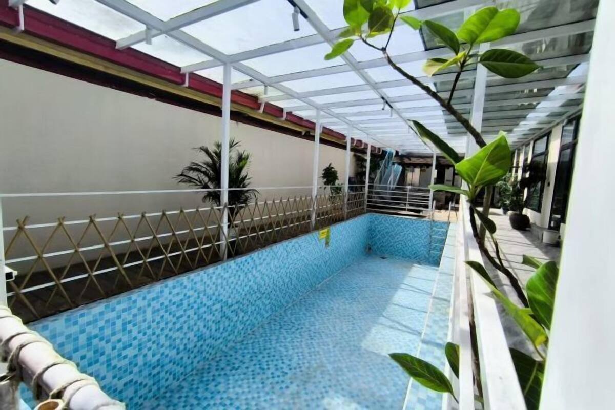An indoor swimming pool with a tiled floor, surrounded by a white fence, and potted plants.