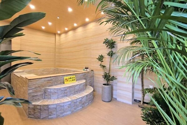Un espace de détente avec un jacuzzi en pierre, entouré de plantes et bordé d’un mur en bois.