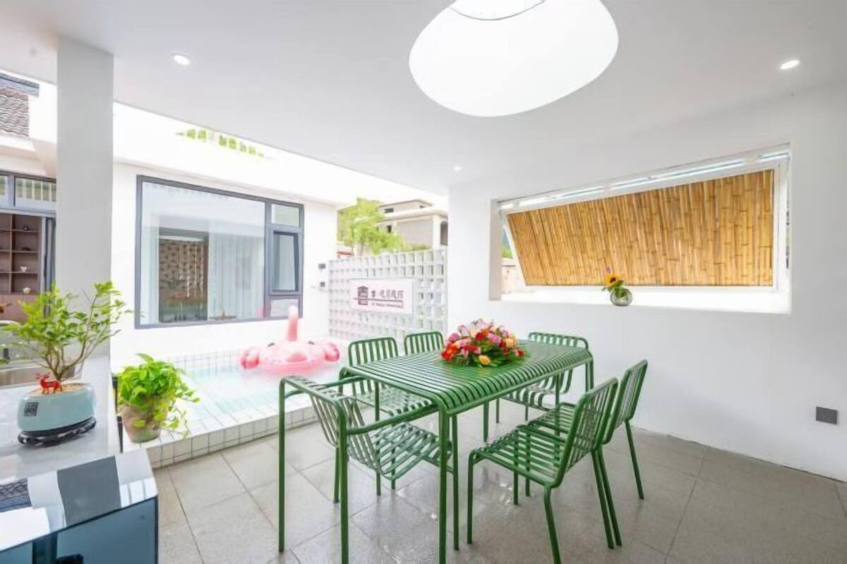 A modern dining area with a green metal table and chairs, a large window with a bamboo blind, and a view of the outside.