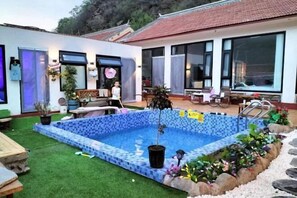 Une piscine dont le bord est revêtu de carrelage, entourée d’un jardin agrémenté de rochers et de plantes.
