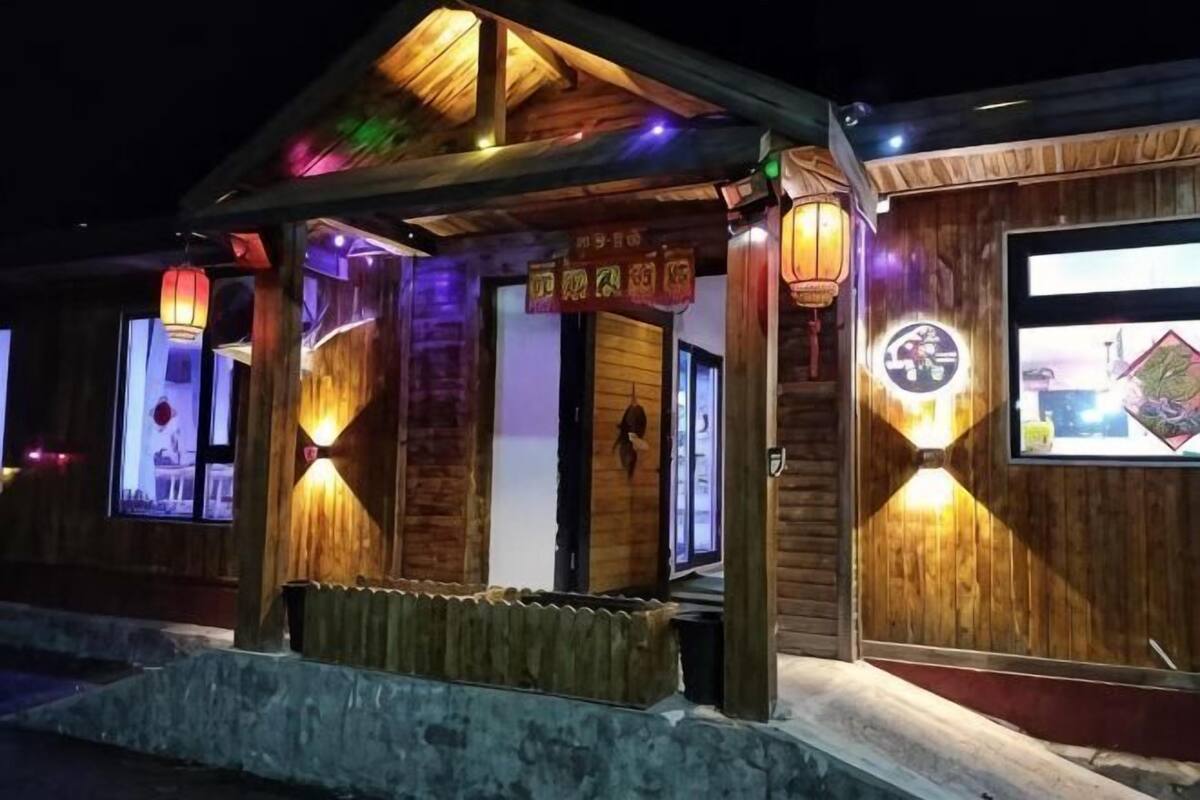 A wooden building with a covered entrance, illuminated by wall-mounted lights, and a bench outside.