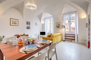 Ein Essbereich mit einem Holztisch, der für eine Mahlzeit gedeckt ist, einer Couch und einem Fernseher im Hintergrund.