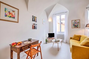 Ein modernes Wohnzimmer mit Essbereich, einer Couch, einem Fernseher auf einem Schrank und Kunstwerken an den Wänden.