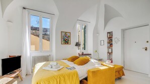 Une chambre d’hôtel avec un lit, un bureau avec une télévision, une bibliothèque et une grande fenêtre.