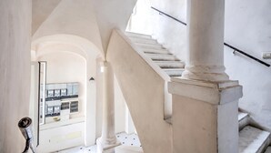 Un escalier orné de colonnes blanches et doté d’une rampe, menant à un niveau supérieur avec un balcon.