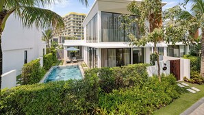 A modern residential building with a swimming pool, lush greenery, and a view of a high-rise building in the background. - Aqua Vista Hoi An Beachfront Villas (Da Nang)