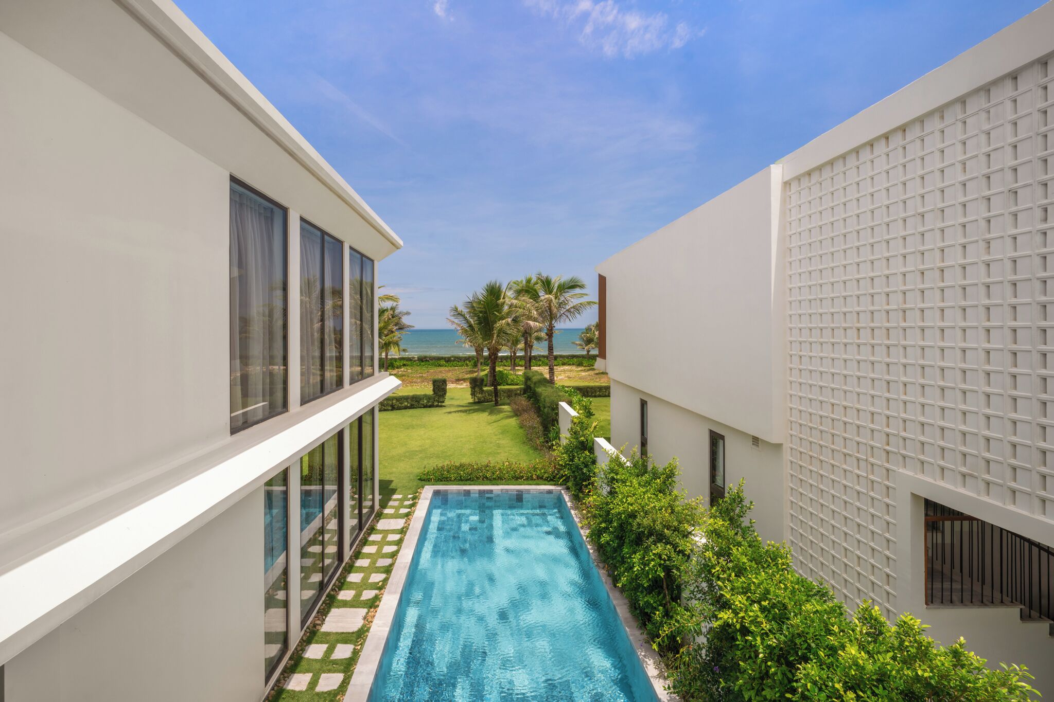 A modern building with a swimming pool, a view of the ocean, and a well-maintained lawn.