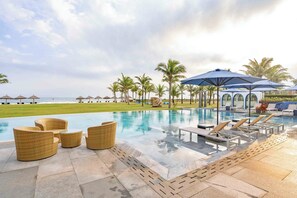 A poolside area with lounge chairs, umbrellas, and a view of the ocean. - Aqua Vista Hoi An Beachfront Villas (Da Nang)