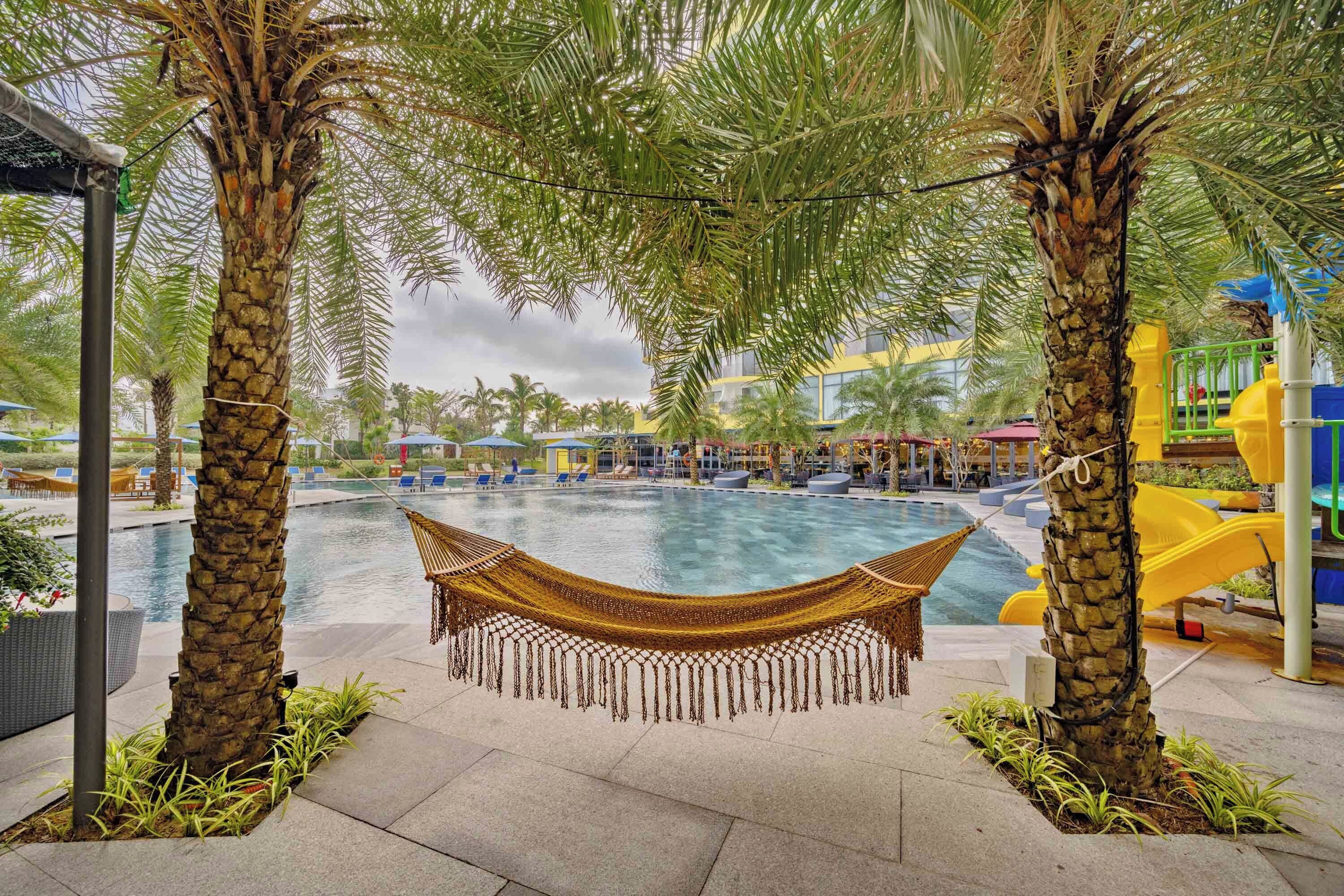 A pool area with a hammock, palm trees, and a children's play area.