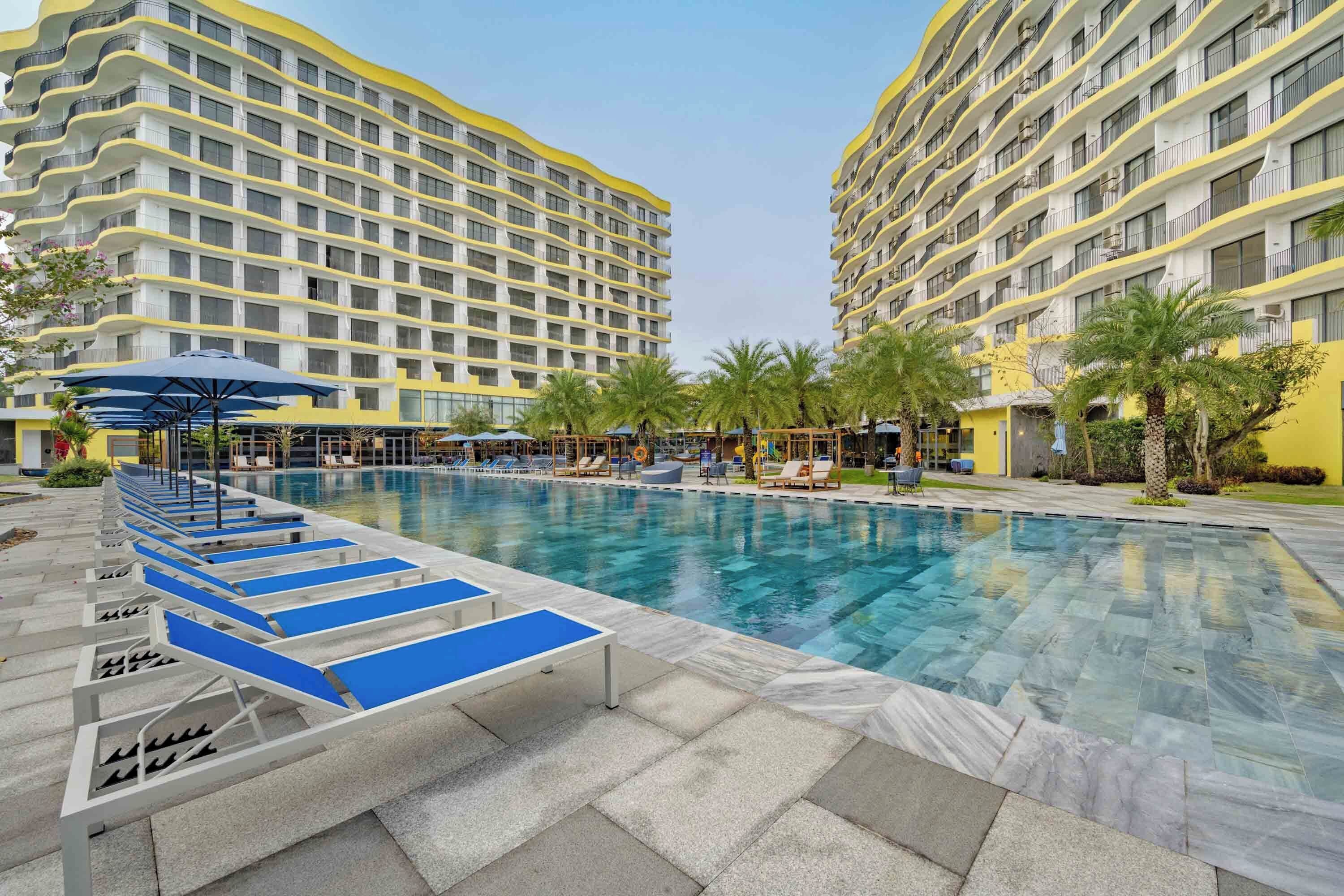 A hotel with a swimming pool, lounge chairs, and palm trees.