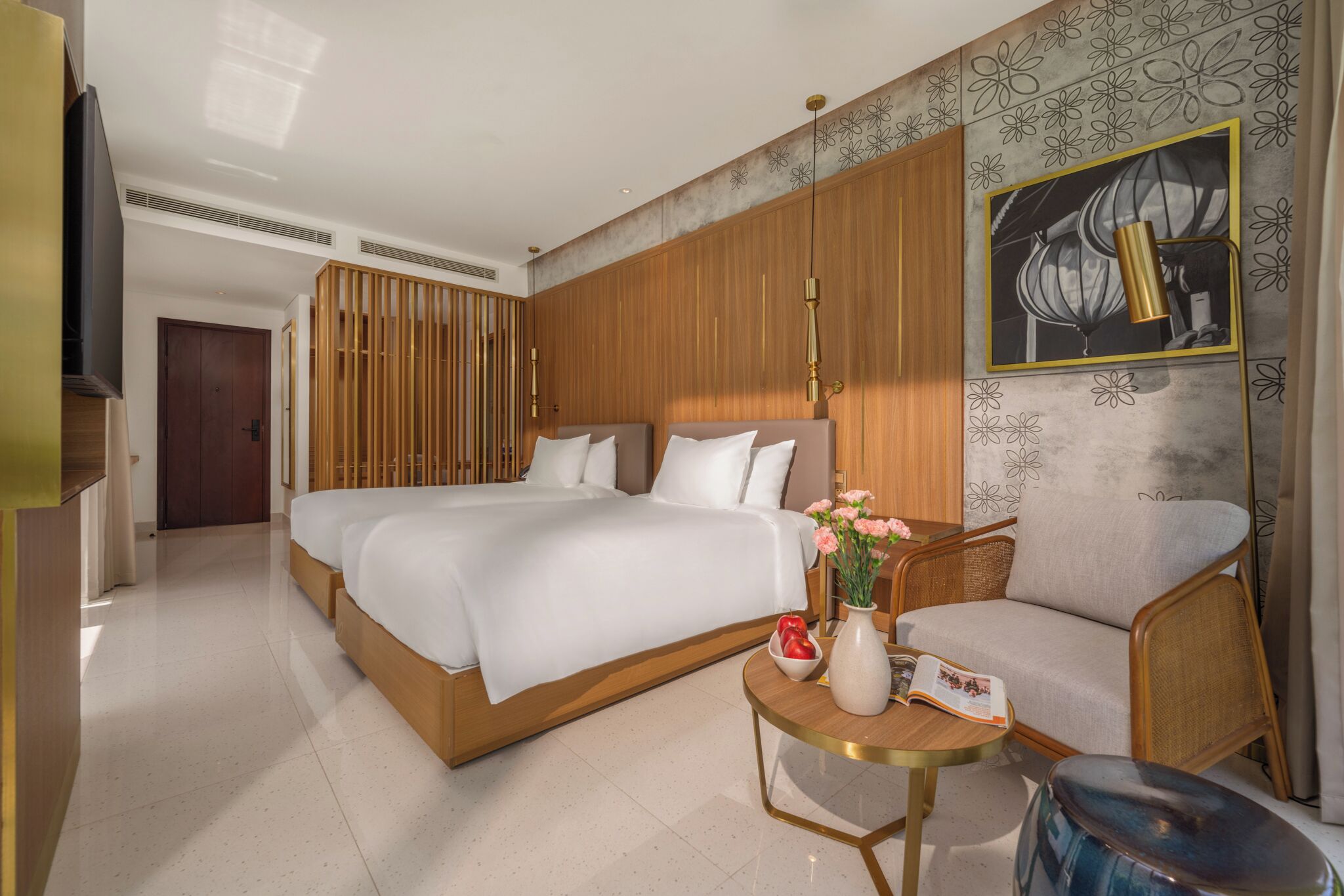 A modern hotel room with a large bed, a sofa, a small table with a vase of flowers, and a painting on the wall.