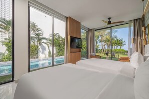 A hotel room with a large bed, a TV, a ceiling fan, and a view of a swimming pool and palm trees. - Aqua Vista Hoi An Beachfront Villas (Da Nang)