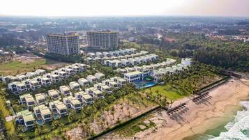 Un resort con varias construcciones tipo bungalow, una playa y un área de piscina.