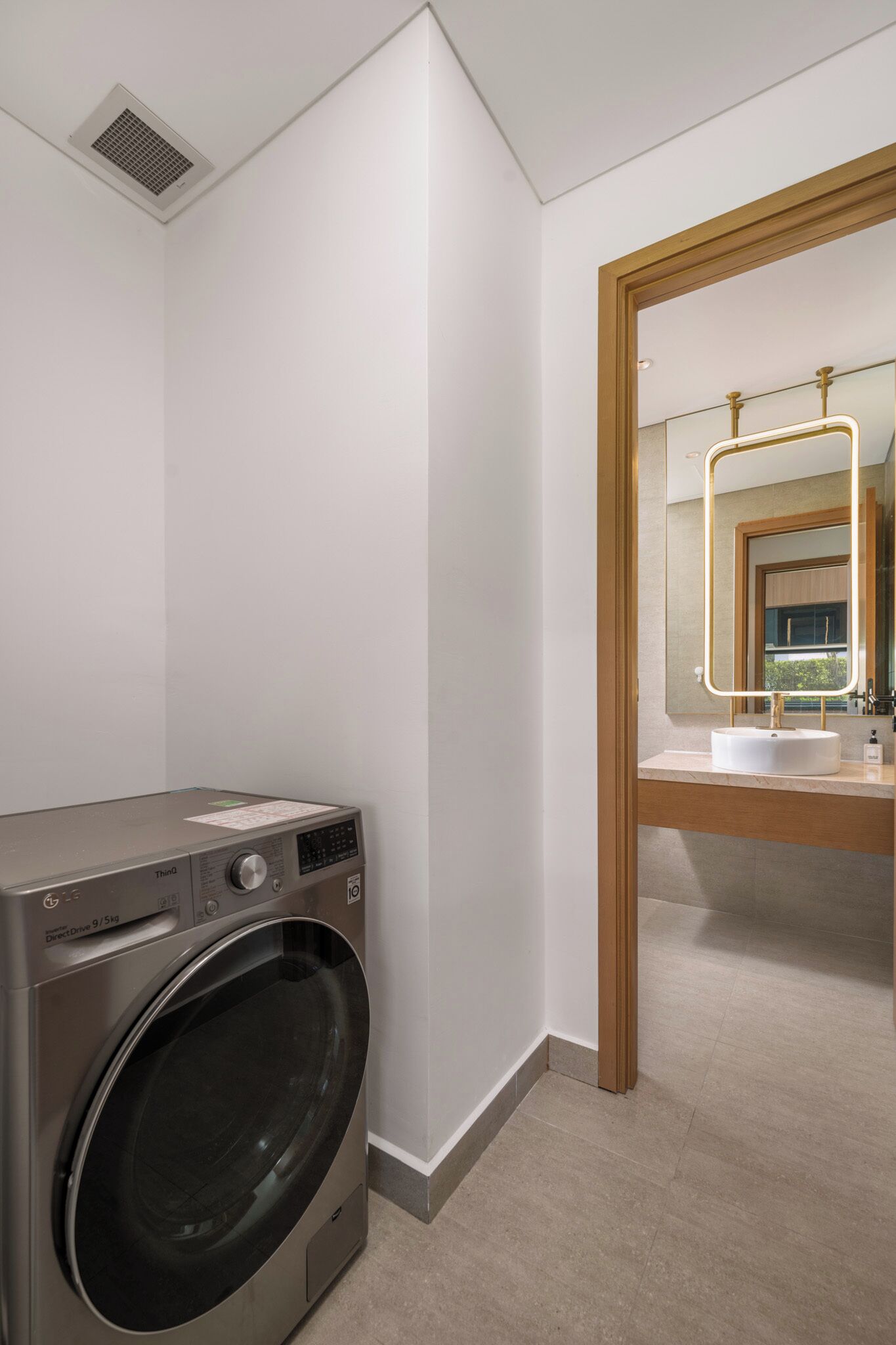 A modern bathroom with a built-in washing machine, a large mirror with a lighted frame, and a sink.