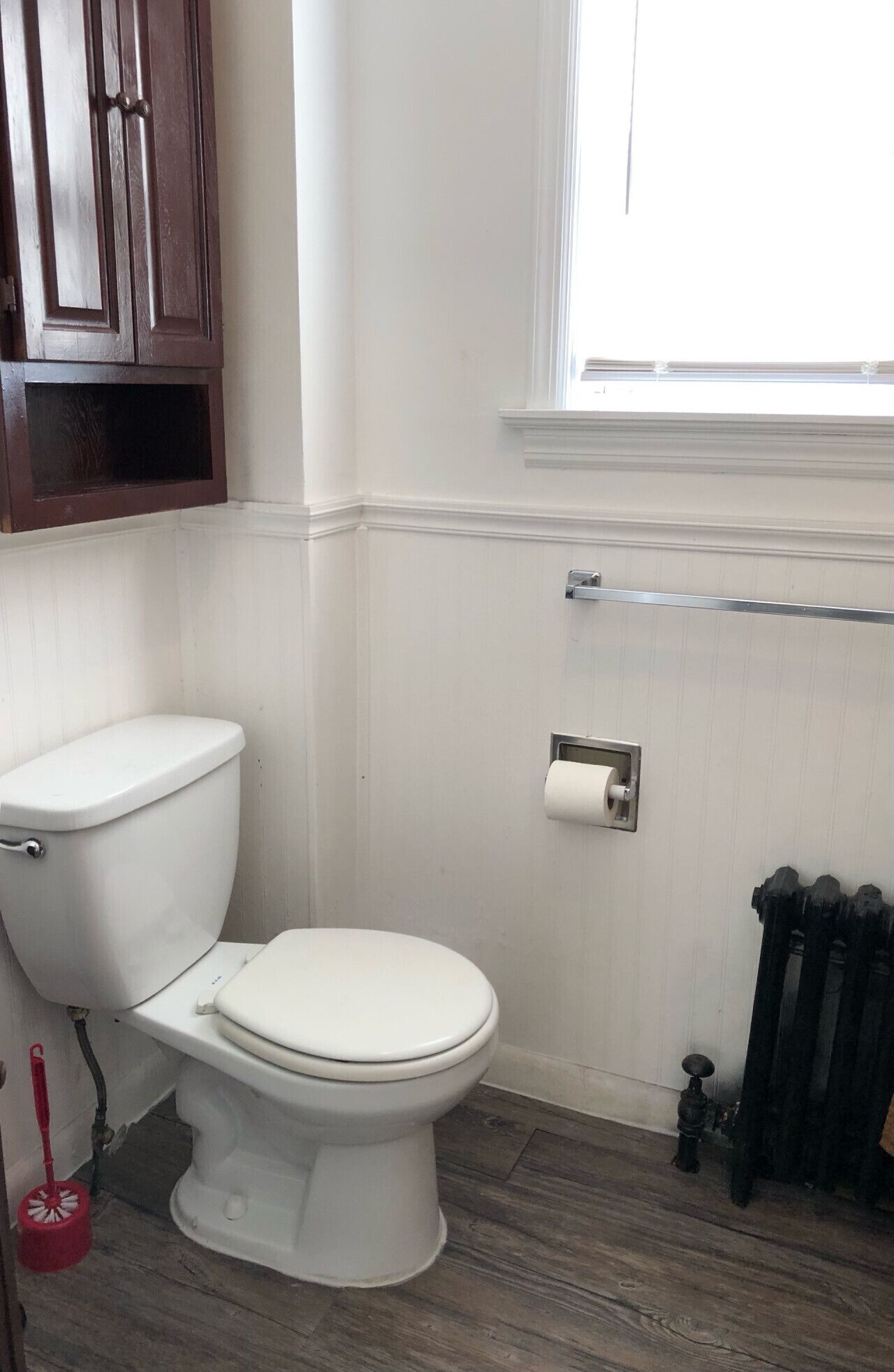 Un baño con inodoro blanco, un armario de madera, una ventana y un radiador.
