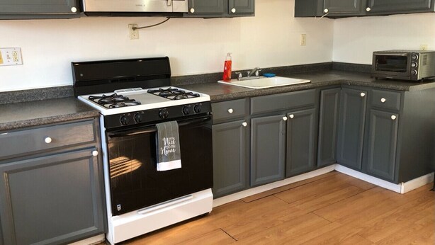 Una cocina con gabinetes gris oscuro, un microondas de acero inoxidable, una estufa a gas y un horno empotrado.