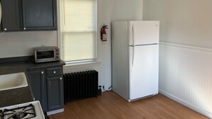 Uma cozinha compacta com fogão a gás, micro-ondas, geladeira e janela com persianas.