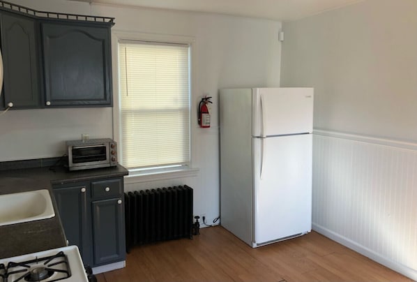 Una pequeña cocina con estufa a gas, microondas, refrigerador y ventana con persianas.