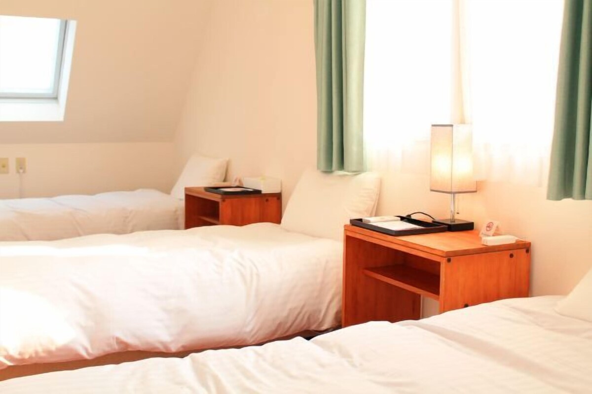 Une chambre d’hôtel avec deux lits, une table de chevet avec une lampe et une fenêtre avec des rideaux.