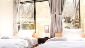 Una camera da letto con due letti, un comodino con una lampada e vista su un'area esterna innevata attraverso ampie finestre.