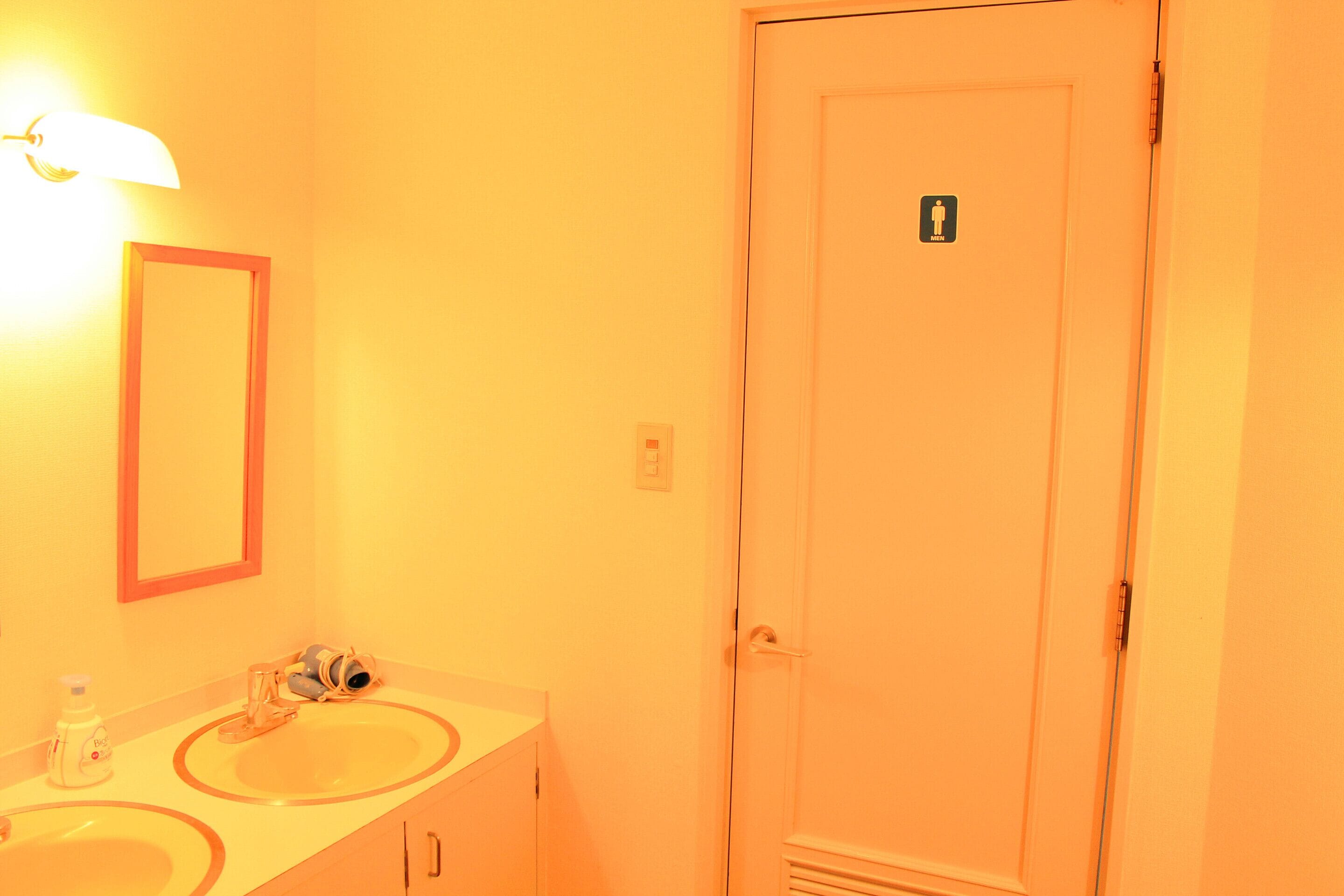 A bathroom with two sinks, a mirror, and a door with a male restroom symbol.