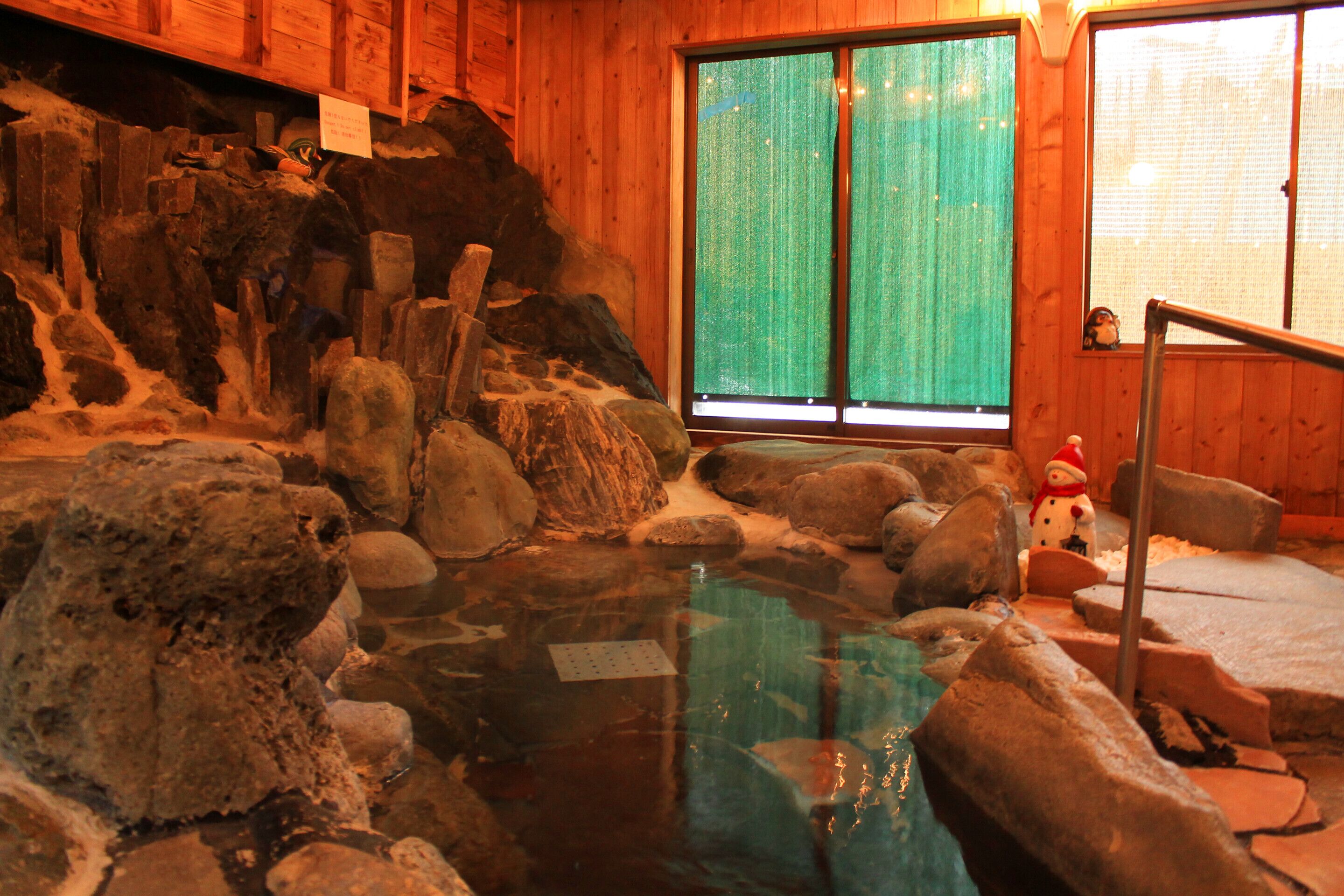 Un área de aguas termales con paredes de madera, una zona de visibilidad con vidrio y una decoración de muñeco de nieve.
