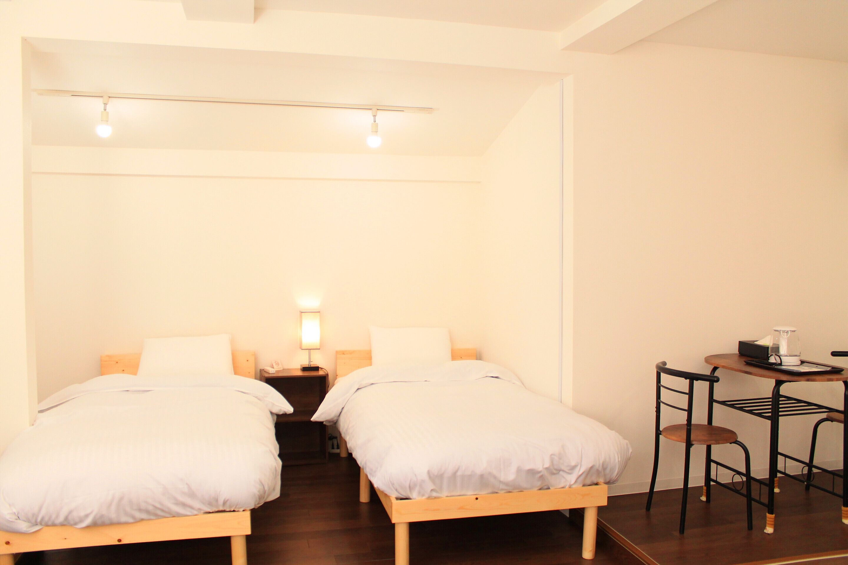 A room with two single beds, a small table with a chair, and a nightstand with a lamp.