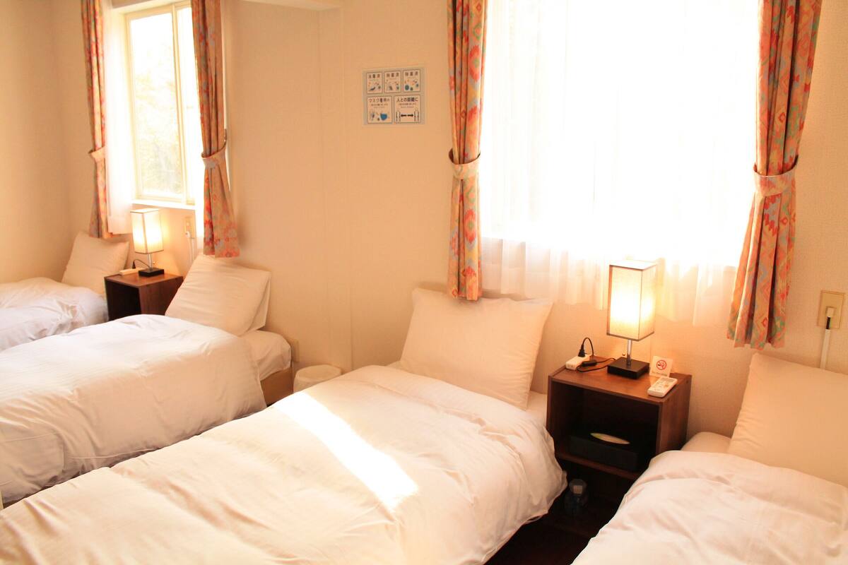 Une chambre d’hôtel avec deux lits simples, une table de chevet avec une lampe et une fenêtre avec des rideaux.