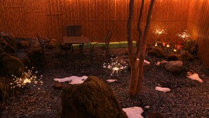 Un giardino interno tranquillo con uno sfondo di bambù, un’area salotto e luci decorative.