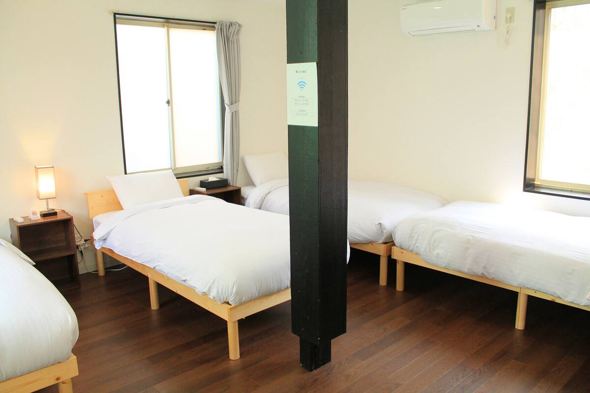 Une chambre d’hôtel avec deux lits simples, une table de chevet avec une lampe, une fenêtre avec des rideaux et un appareil de climatisation fixé au mur.