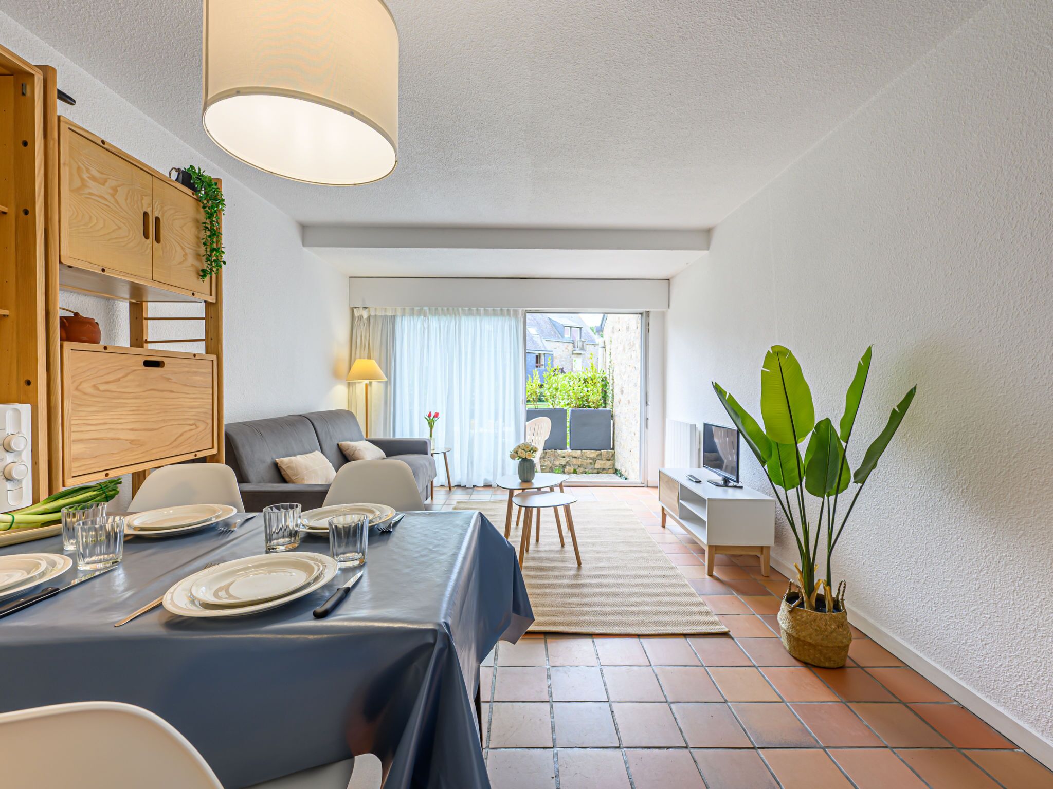 A modern living room with a dining area, a sofa, a TV stand, and a large plant.