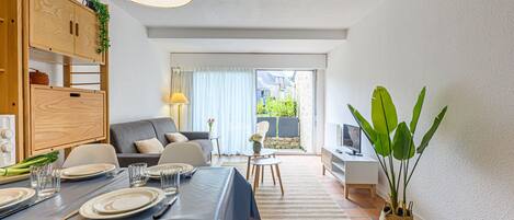 A modern living room with a dining area, a sofa, a TV stand, and a large plant.