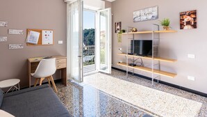 A modern room with a desk, chair, and TV. There's a large window with a view of trees and buildings. - Casa della Nonna Gilda by Interhome (Sanremo)