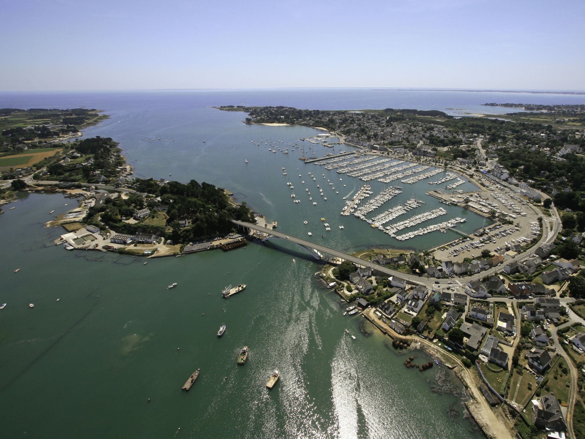 An aerial view of a coastal town with a marina, a bridge connecting the mainland to an island, and residential areas.