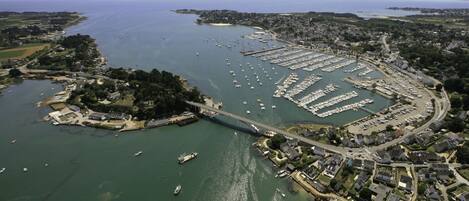 An aerial view of a coastal town with a marina, a bridge connecting the mainland to an island, and residential areas.