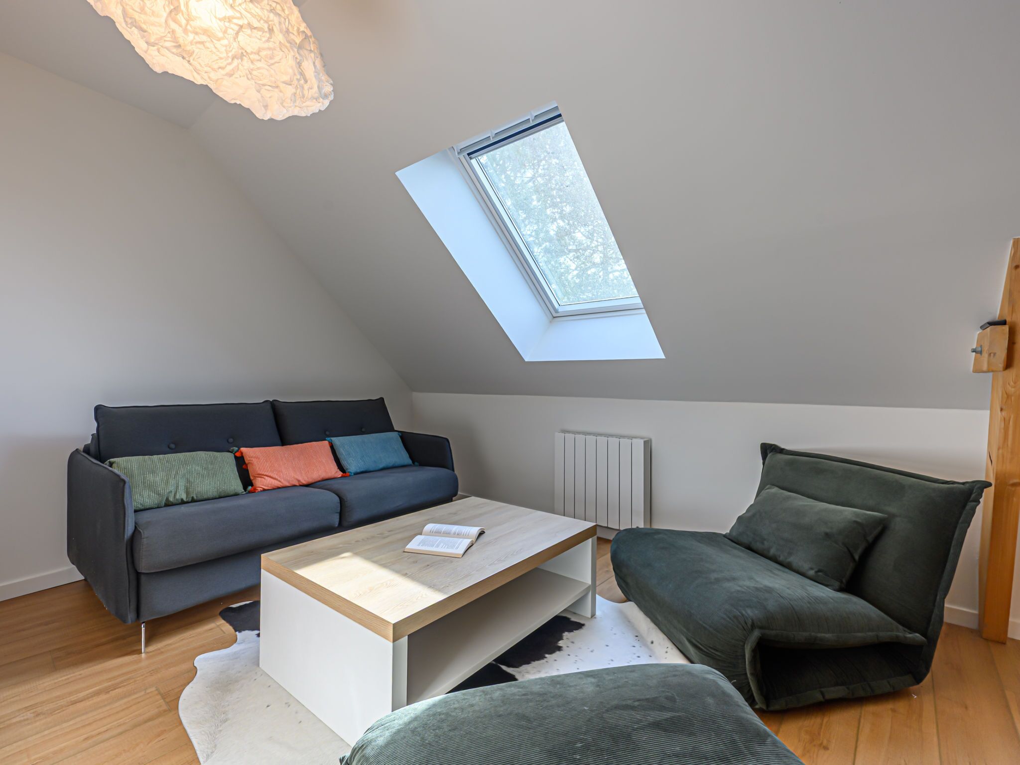 Une chambre de style loft moderne avec un plafond en pente, une lucarne, un canapé gris foncé, une table basse en bois et un fauteuil vert.