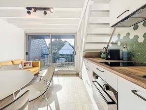 A modern kitchen with a large window, a dining area with a white table and chairs, and a yellow sofa with a 'BON HEUR' pillow. - Phare de Kernevest by Interhome (Saint Philibert)