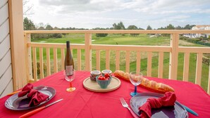 A balcony table set with a bottle of wine, glasses, a baguette, and a bowl of cherries. - L'Orée du Golf by Interhome (Pornic)
