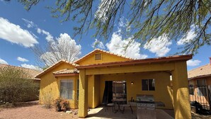A yellow house with a patio, a grill, and a covered seating area.