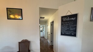 A hallway with a welcome sign, a wicker chair, and a framed picture on the wall.