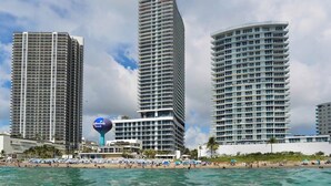 Tres hoteles de gran altura con balcones, una playa en primer plano y un cielo despejado.